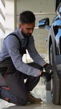 Profesyonel bir tamirci modern bir atölyede araba tekerleğini sıkarken diz çöker ve düzgün bir bakım ve araç güvenliği sağlar..