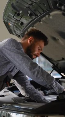 Profesyonel bir oto tamircisi modern bir araç hizmet merkezinde açık kaputun altında araba motorunu dikkatle kontrol eder ve tamir eder..