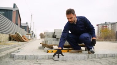 Donanma üniformalı bir inşaat işçisi, konağın yakınındaki kaldırıma kaldırım taşları yerleştiriyor. Plastik bir çekiç ve ruh seviyesi kullanıyor..
