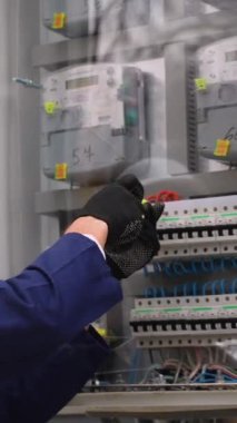 Beyaz bir şapka ve eldiven takan profesyonel bir elektrikçi bir inşaat alanında açık hava elektrik paneli kuruyor ve ayarlıyor..