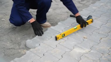 Mavi tulumlu bir inşaat işçisi, yol kenarındaki taşları sarı bir ruh seviyesiyle birbirine kenetliyor..