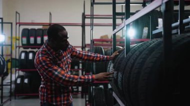 Afrika kökenli bir Amerikalı bir oto yedek parça dükkanında lastik seçiyor ve bir satış elemanını satın almasına yardım etmesi için çağırıyor..