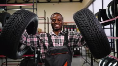 Tulumlu neşeli bir Afrikalı Amerikalı işçi otomotiv dükkanındaki halterler gibi iki tekerleği kaldırıyor ve iş yerinde eğleniyor..