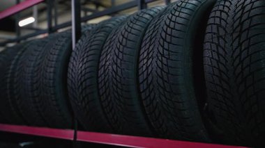Bir otomotiv mağazasında ya da lastik servis merkezinde metal bir rafa düzgün yerleştirilmiş siyah araba lastikleri..