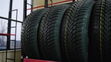 Detaylı lastik izleri ve sarı kılavuz çizgileri olan çivili kış lastikleri bir otomotiv mağazasındaki metal askıda satılmaya hazır..