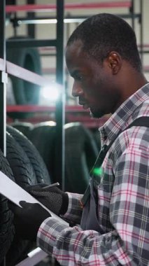 Ekose gömlekli ve eldivenli bir işçi deponun tekerlerini incelerken envanter sayımını da not ve kalem kullanarak yapıyor.