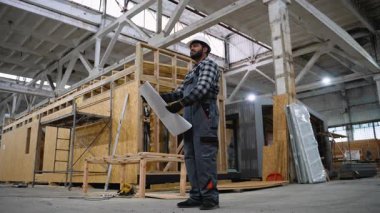 Sert bir şapka ve eldiven takan Hintli bir mühendis, büyük bir üretim tesisinde modüler evler inşa edilirken planları inceliyor..