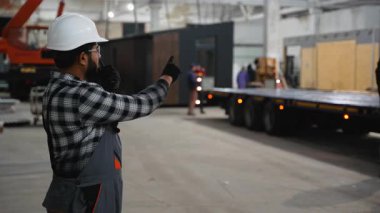 Sert şapka ve eldiven takan Hintli bir inşaat işçisi modüler bir evin karavana yüklenmesini koordine etmek için telsiz kullanıyor.