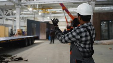 Hintli bir inşaat işçisi modüler bir evin yükünü vinçli bir karavana yönlendirmek için telsiz kullanıyor.