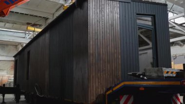 Karanlık ahşap panelli modern prefabrik modüler bir ev güvenli bir şekilde bir nakliye karavanına yerleştirilir. Teslimata hazır..