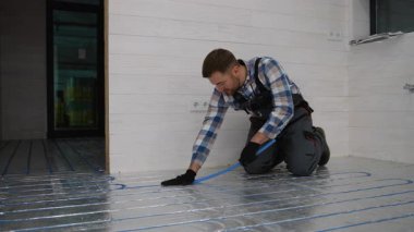 Zeminde diz çökmüş bir inşaat işçisi prefabrik modüler bir eve bir alt kat ısıtma sistemi kuruyor, düzgün yalıtım ve kablolama sağlıyor..