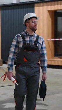 Güvenlik teçhizatı olan bir inşaat işçisi, modern prefabrikasyondaki üretim ve kalite kontrolünü denetleyen bir modüler ev fabrikasında yürüyor..