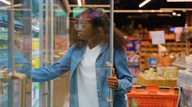 Genç Afrikalı Amerikalı ev hanımı mandıra bölümünden yumurta seçmek için markette soğutulmuş cam bir kapı açıyor..