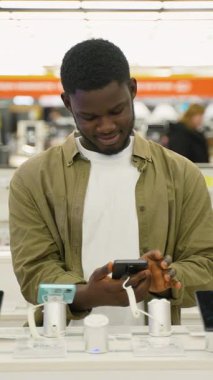 Genç bir Afrikalı Amerikalı, bir teknoloji mağazasında akıllı telefonu inceliyor. Model ve özelliklerini karşılaştırıyor..