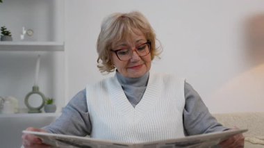 Gözlüklü yaşlı kadın rahat bir koltukta oturup gazete okuyor. Odaklanmış ve meşgul görünüyor. Evdeki son gelişmelerden haberdar..