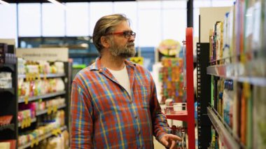 Ekose gömlekli yaşlı bir adam satış sırasında bir mağazadan oda parfümü seçer, süpermarketten alışveriş yaparken dikkatlice bir ürün seçer..