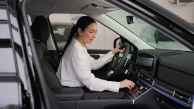 Beyaz gömlekli mutlu bir kadın modern siyah bir arabanın sürücü koltuğunda oturur, müzik dinler ve dans eder..