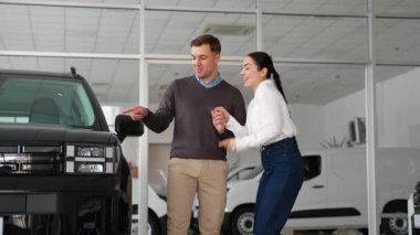 Mutlu bir çift, yeni siyah arabalarının yanında galeride gülümsüyor ve başarılı alışverişlerini ve yeni heyecanlı yolculuklarını kutluyor..