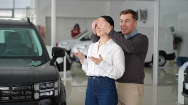 Bir adam bir bayanın gözlerini kapatır ve bayilikte yeni bir arabayla sürpriz yapar. Lüks bir aracın yanında durarak heyecanla ve heyecanla tepki veriyor..