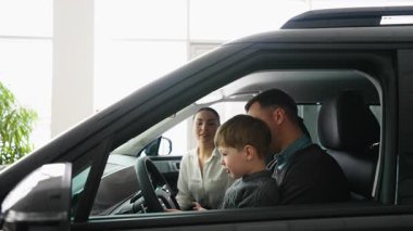 Mutlu bir aile galeride yeni bir arabanın içinde oturup özelliklerini kontrol eder. Baba, anne ve oğul satın almadan önce aracı keşfetmekten zevk alır..