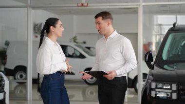 Bir araba satıcısı yeni bir aracın anahtarlarını verir ve bir galerinin içinde kadın bir müşteriyle tokalaşır ve satış anlaşmasını sonuçlandırır..