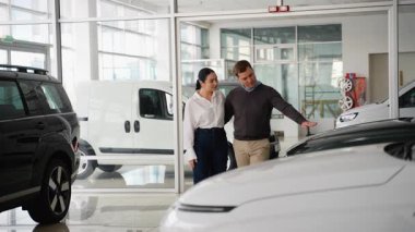 Genç bir çift seçenekleri değerlendiriyor ve ayrıntıları tartışırken modern bir galeride çeşitli araçları olan yeni bir araba seçiyor..