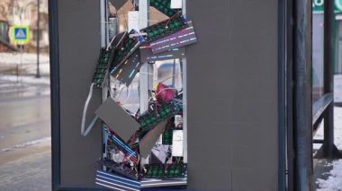 Kırık LED panelleri olan bir otobüs durağındaki ağır hasarlı dijital reklam panosu, açığa çıkmış elektronik devreler, ve karlı bir caddede karışık kablolar..