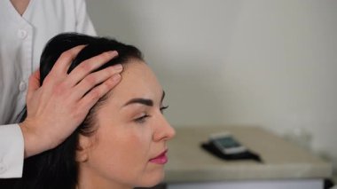 Bir tricholog, saç tedavi seansı sırasında bir kadının kafa derisine nazikçe masaj yapar. Kafa masajı kan dolaşımını, saç büyümesini ve genel olarak kafa derisi sağlığını iyileştirmeye yardımcı olur..