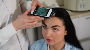 Bir tricholog, kepek, saç dökülmesi, deri dökülmesi ve kafa derisi hastalıklarını teşhis etmek için akıllı telefon bağlantılı dijital büyüteç kullanan bir kadının kafa derisini analiz eder..