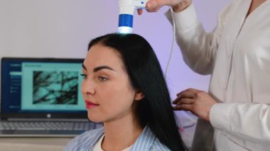 Bir kadın dijital bir cihaz kullanarak kafa derisini incelemek için bir trikoloğu ziyaret ediyor. Bu prosedür saç dökülmesi, kepek, sebora ve kafa derisi hastalıklarının teşhis edilmesine yardımcı oluyor..