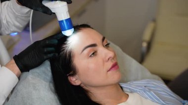 Bir kadın dijital bir cihaz kullanarak kafa derisini incelemek için bir trikoloğu ziyaret ediyor. Bu prosedür saç dökülmesi, kepek, sebora ve kafa derisi hastalıklarının teşhis edilmesine yardımcı oluyor..