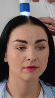 Bir kadın dijital bir cihaz kullanarak kafa derisini incelemek için bir trikoloğu ziyaret ediyor. Bu prosedür saç dökülmesi, kepek, sebora ve kafa derisi hastalıklarının teşhis edilmesine yardımcı oluyor..