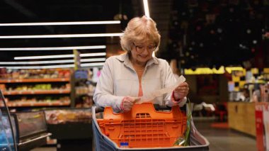 Gözlüklü yaşlı bir kadın, artan gıda fiyatları ve enflasyona tepki olarak süpermarket koridorundaki uzun market fişini kontrol ederken şaşırmış görünüyor..