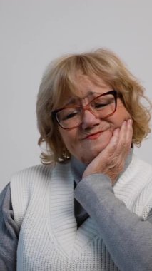 Son sınıf öğrencisi bir kanepede oturuyor, yanağını acı dolu bir ifadeyle tutuyor, muhtemelen diş ağrısı, çene ağrısı ya da diş ağrısı çekiyor..