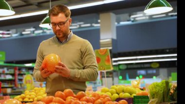 Bir adam marketin sebze reyonundan taze narenciye alırken bir torba greyfurtu teftiş eder..