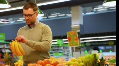 Bir adam marketin sebze reyonundaki ananas gibi taze tropikal meyve alırken bir sürü muzu teftiş eder..