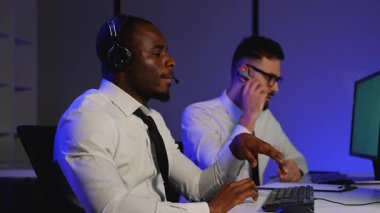 Kulaklık takan iki lojistik sevkiyat görevlisi, nakliyeleri izlemek, rotaları optimize etmek ve verimli teslimatları sağlamak için birden fazla monitör kullanarak nakliye işlemini yönetiyor..