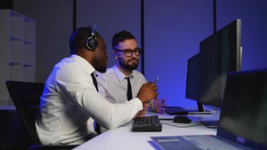 Bir veri merkezindeki iki bilişim operatörü birden fazla monitördeki büyük verileri tartışıyor. Ticari ve teknolojik operasyonlar için karmaşık bilgileri analiz edip yönetirler..