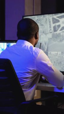 Bir güvenlik subayı, radyo ile konuşurken kontrol odasında birden fazla güvenlik kamerası görüntüsü izler. Güvenlik ve güvenliği sağlamak için talimatlar verir..