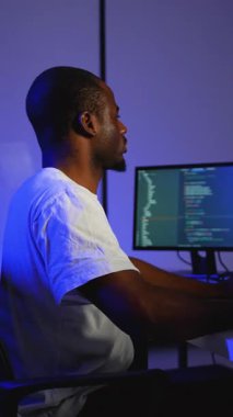 Bir yazılım geliştiricisi loş ışıklı bir ofiste çift monitörlerde programlama, siber güvenlik ve yazılım geliştirme üzerine çalışarak kod yazar ve hata ayıklar.