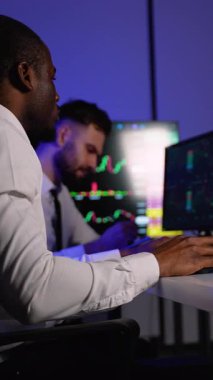 Beyaz gömlekli odaklı bir borsa simsarı birden fazla ekranda finansal grafikleri izler, pazar eğilimlerini analiz eder ve modern bir ofiste yatırım kararları alır..