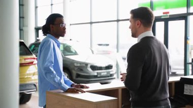 Bir araba satıcısı, modern bir galeride tatmin olmuş bir müşteriyle el sıkışırken yeni bir arabanın anahtarlarını teslim eder..