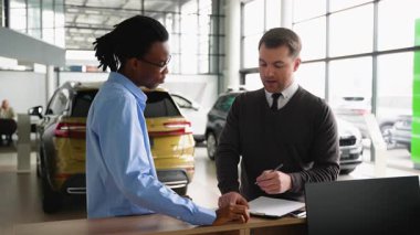 Bir araba satıcısı, satış mağazasındaki bir müşteriye indirimli araç anlaşmasını açıklar. Satın alma işlemini bitirmeden önce sözleşmeyi gözden geçirir..