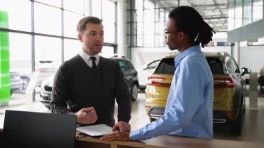 Bir araba satıcısı bir satın alma sözleşmesi imzalar ve modern bir galerideki bir müşteriye yeni bir aracın anahtarlarını teslim eder..