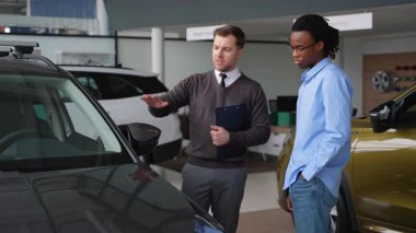 Bir araba satıcısı, bir galerideki potansiyel alıcıya bir aracın özelliklerini açıklar ve karar verme sürecine yardımcı olur..