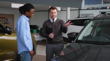 Bir araba satıcısı, bir galerideki potansiyel alıcıya bir aracın özelliklerini açıklar ve müşteriye bilgilendirilmiş bir satın alma kararı almasında yardımcı olur..