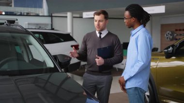 Bir araba satıcısı, bir galeride Afro-Amerikalı bir müşteriye satış yapmadan önce özellikleri ve satın alma seçeneklerini tartışan bir araç sunar..