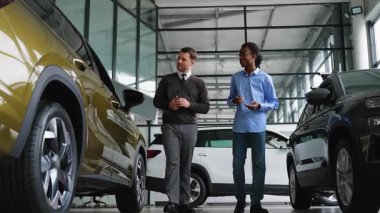 Araba satıcısı müşteriye galeride araç seçmesinde yardımcı olur. Potansiyel alımlar için özellikler, fiyatlandırma ve finansman seçeneklerini tartışır..