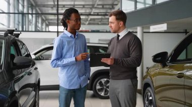 Bir araba satıcısı, bir galeride Afrikalı Amerikalı bir müşteriye indirim teklifi sunar. Anlaşmayı sonuçlandırmadan önce fiyatlandırmayı ve özellikleri tartışır..