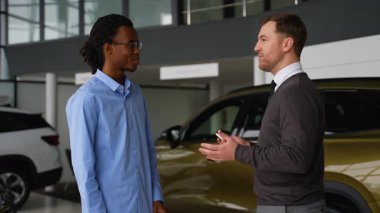 Bir araba satıcısı bir galeride el sıkışırken müşterinin anahtarlarını teslim eder. Araç alımını başarılı bir anlaşmayla sonuçlandırır..
